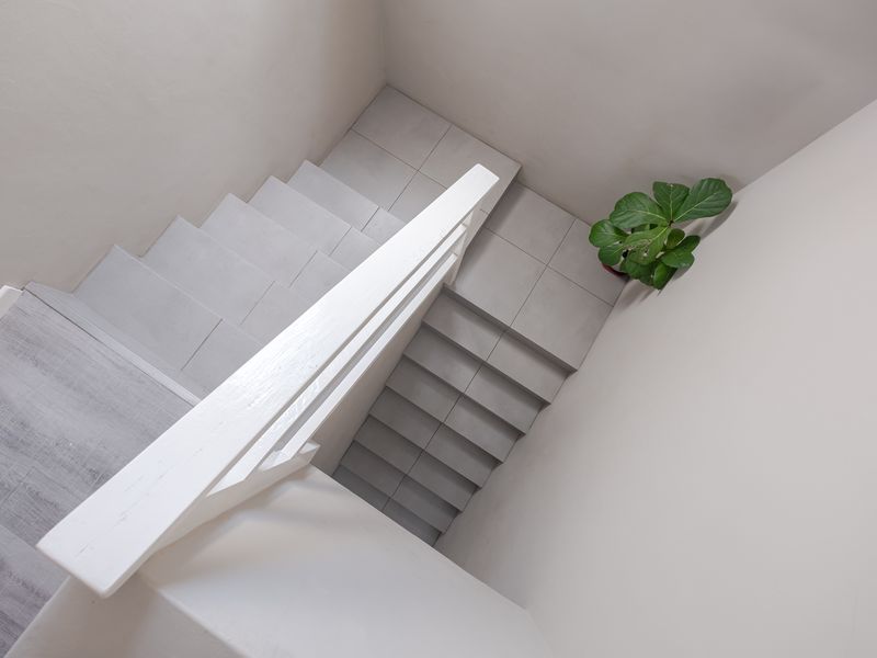 A clean, modern staircase featuring light-toned tiled steps and a white painted wooden handrail, providing a bright and minimalist transition between levels.