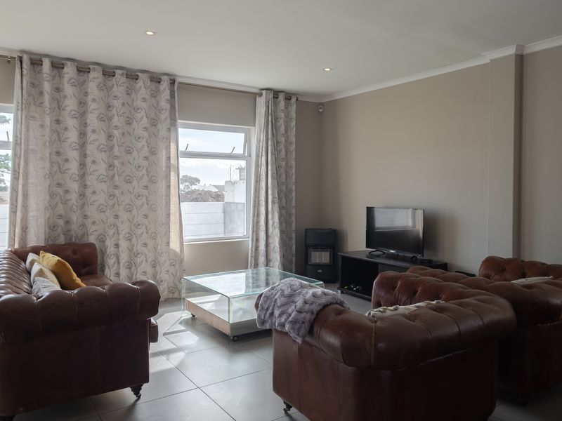 A well-lit living room featuring neutral tiled flooring, recessed downlights, and a built-in gas heater, offering a comfortable and functional space.