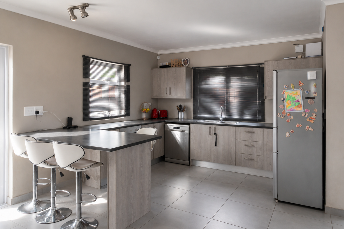 A functional kitchen featuring light wood-grain cabinetry, dark countertops, a breakfast nook, and tiled flooring, complemented by natural light from dual windows.