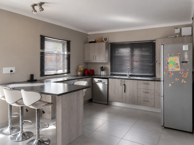 A functional kitchen featuring light wood-grain cabinetry, dark countertops, a breakfast nook, and tiled flooring, complemented by natural light from dual windows.