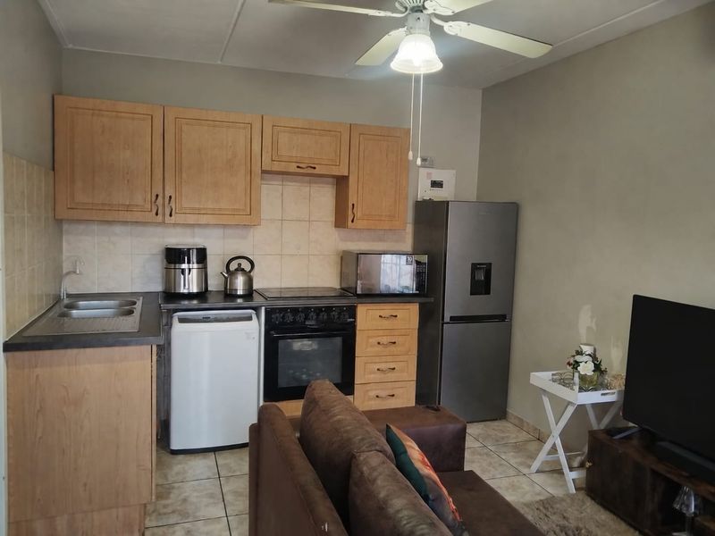 Open-plan kitchen and living area featuring wooden cabinetry, tiled flooring, and a functional layout with integrated cooking appliances.