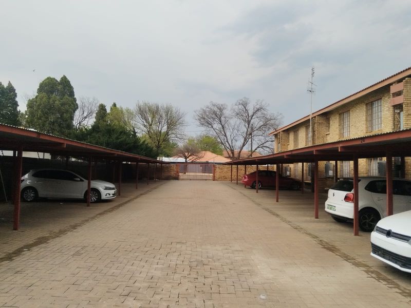A paved outdoor parking area featuring covered carports alongside a brick apartment building.