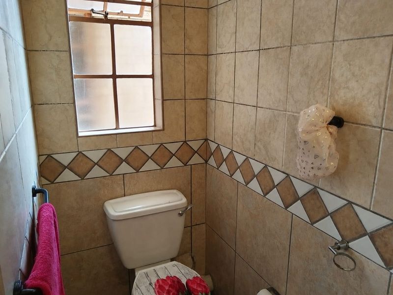 A functional bathroom featuring neutral ceramic wall tiles with a decorative border, a standard toilet, and a small casement window for natural light.