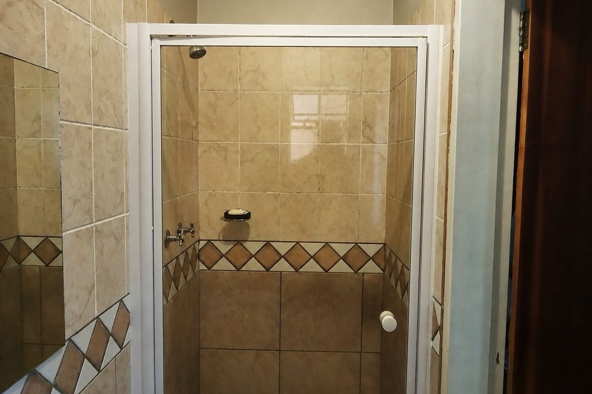 A functional bathroom shower enclosure featuring neutral ceramic wall tiles with a decorative border and a white-framed glass door.