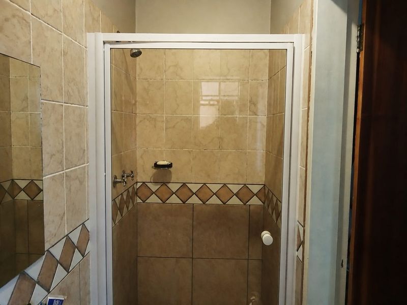 A functional bathroom shower enclosure featuring neutral ceramic wall tiles with a decorative border and a white-framed glass door.