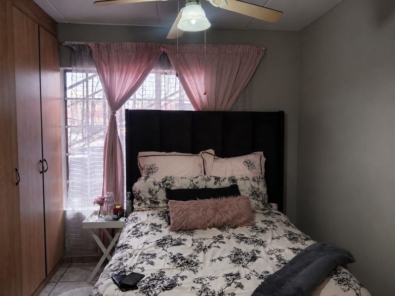 A cozy bedroom featuring built-in wooden wardrobes, a ceiling fan, and tiled flooring, with security bars installed on the window.