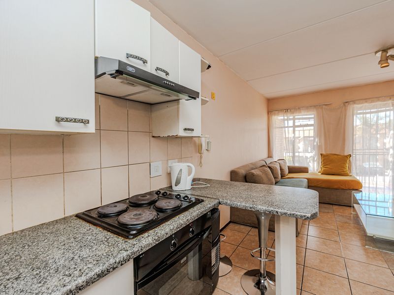 Open-plan kitchen and living area featuring granite countertops, built-in oven and hob, tiled flooring, and direct access to an outdoor patio area.