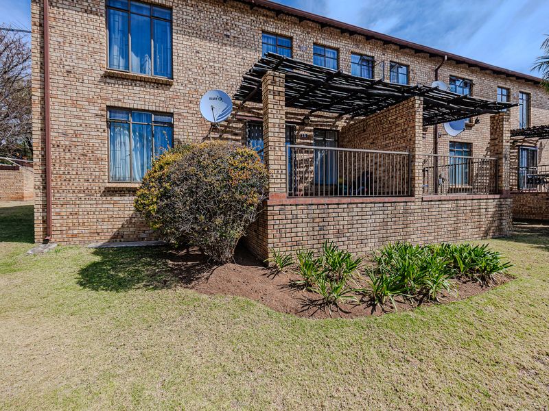 Rear view of a face brick apartment building featuring a private patio with a timber pergola and metal balustrade overlooking a landscaped garden area.
