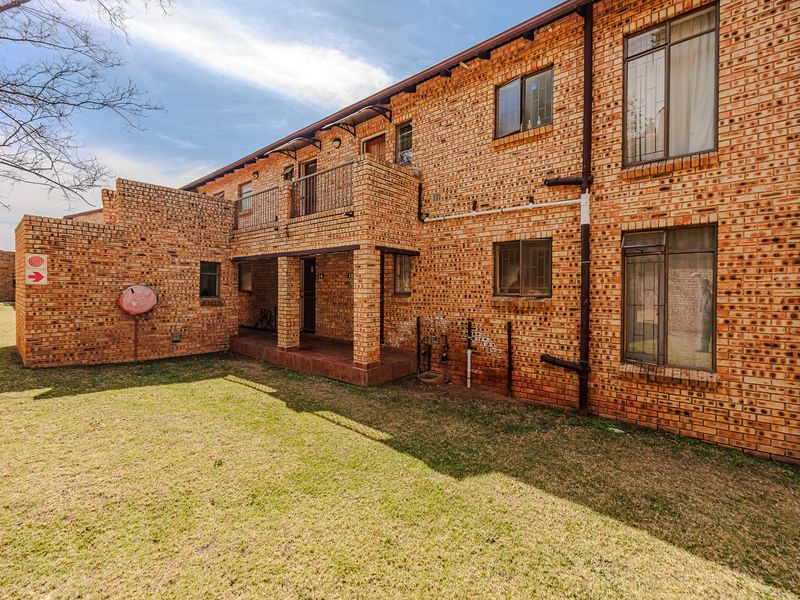 Rear view of a face brick apartment building featuring a ground floor patio, upper-level balcony, and surrounding lawn area.