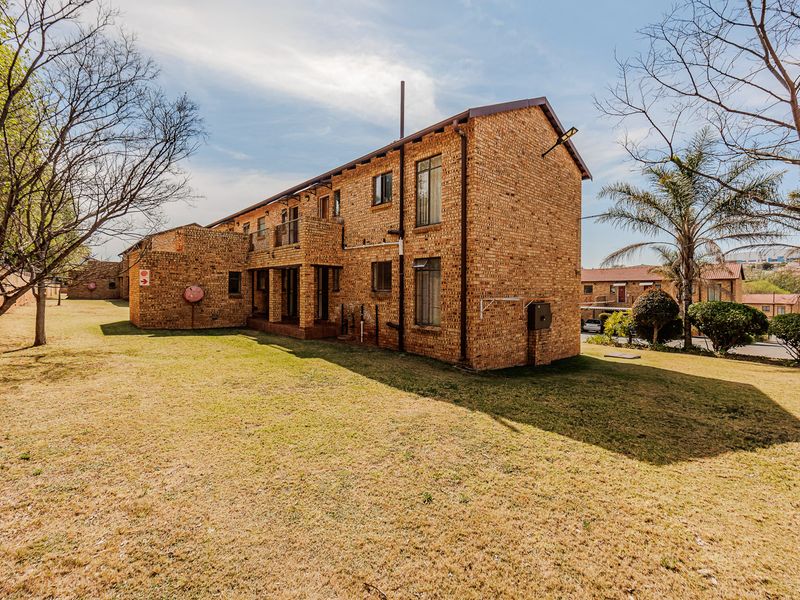 Rear view of a multi-story face brick apartment building featuring balconies and established surrounding garden space.