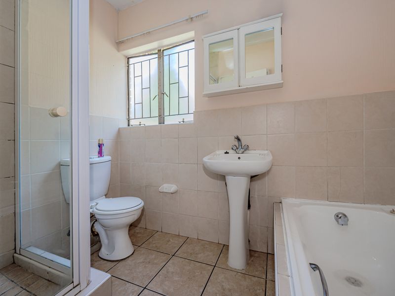 A functional bathroom featuring a pedestal basin, toilet, bathtub, and separate shower enclosure with neutral wall and floor tiling.