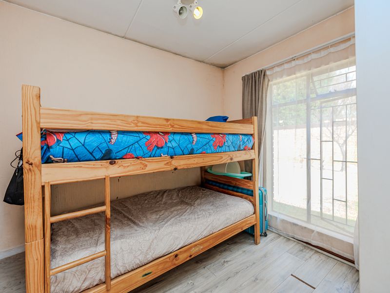 A bedroom featuring tiled flooring and a large window with a security gate, showing signs of wear on the ceiling and walls.