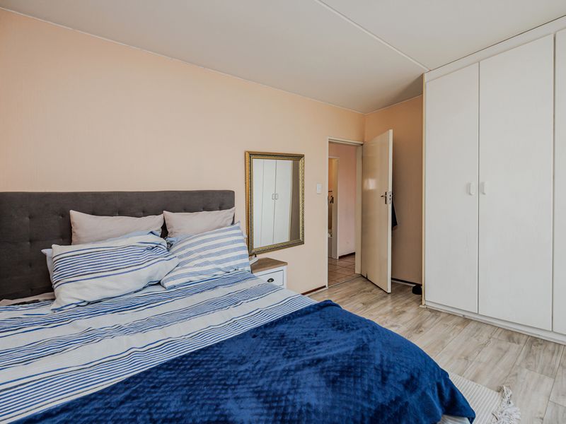 A bedroom featuring light-toned laminate flooring and a large white built-in wardrobe, with access to an adjoining room.