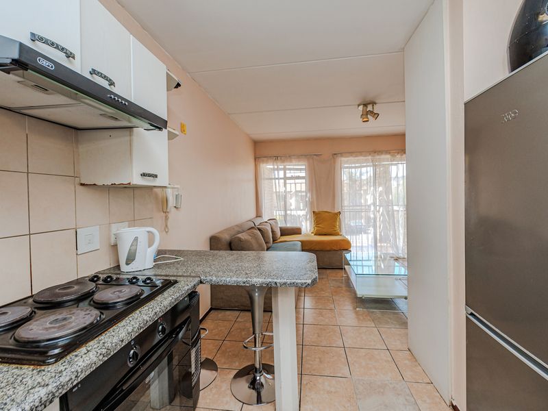 Open-plan living area featuring a functional kitchen with granite countertops, electric hob, and tiled flooring, leading to a bright living space with balcony access.
