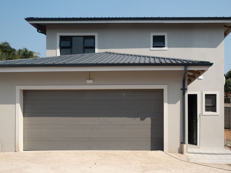 Front elevation of a modern townhouse featuring a large sectional garage door, metal roofing, and clean exterior finishes.