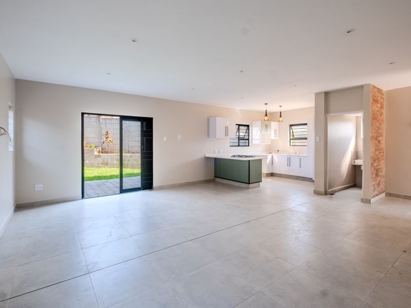 Spacious open-plan living and kitchen area featuring tiled floors, modern cabinetry, a gas hob, and an exposed brick accent wall leading to the garden.
