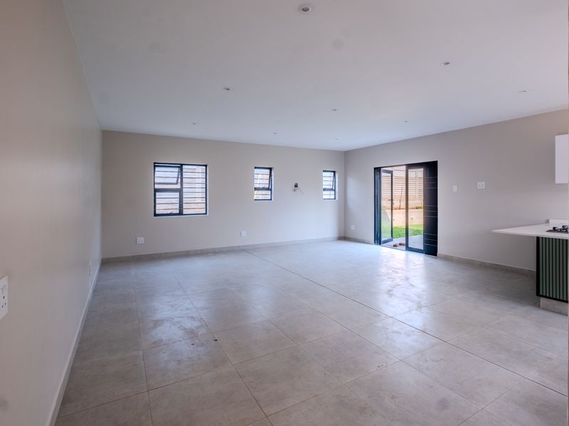 Spacious open-plan living area featuring neutral tiled flooring, recessed lighting, and direct access to the garden through sliding glass doors.