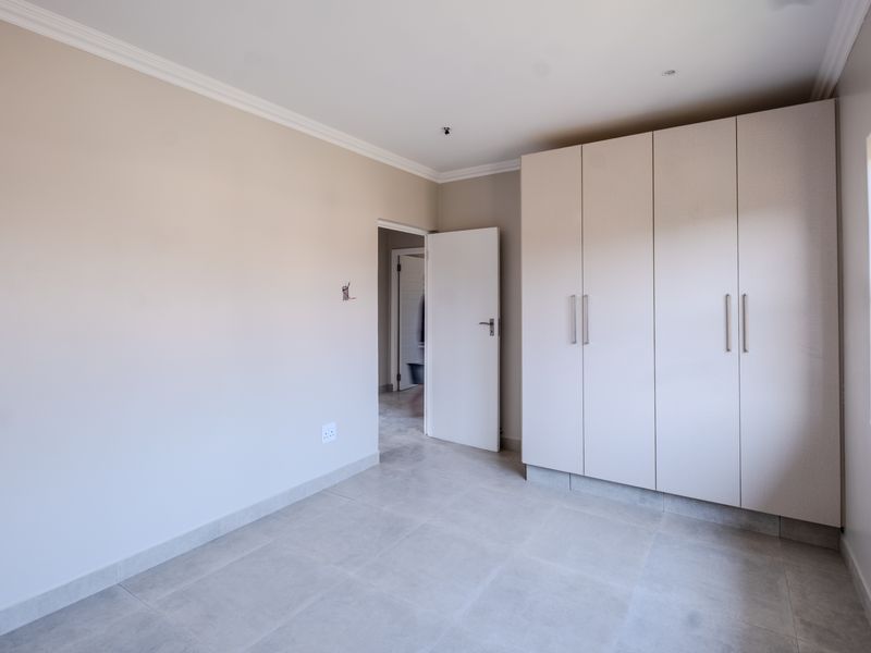 A clean, empty bedroom featuring neutral tiled flooring, built-in cupboards, and crisp white walls, ready for personalization.