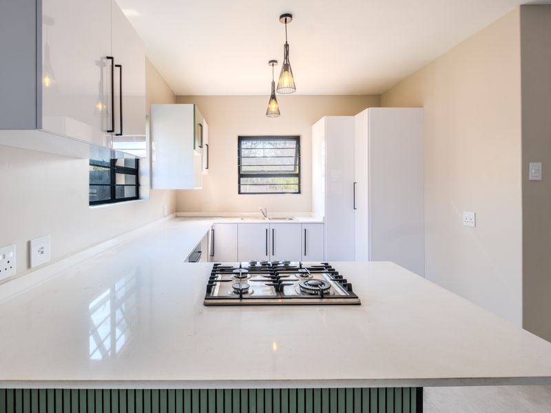 Modern kitchen featuring sleek white cabinetry, quartz countertops, a built-in gas hob, and contemporary pendant lighting in a clean, minimalist space.
