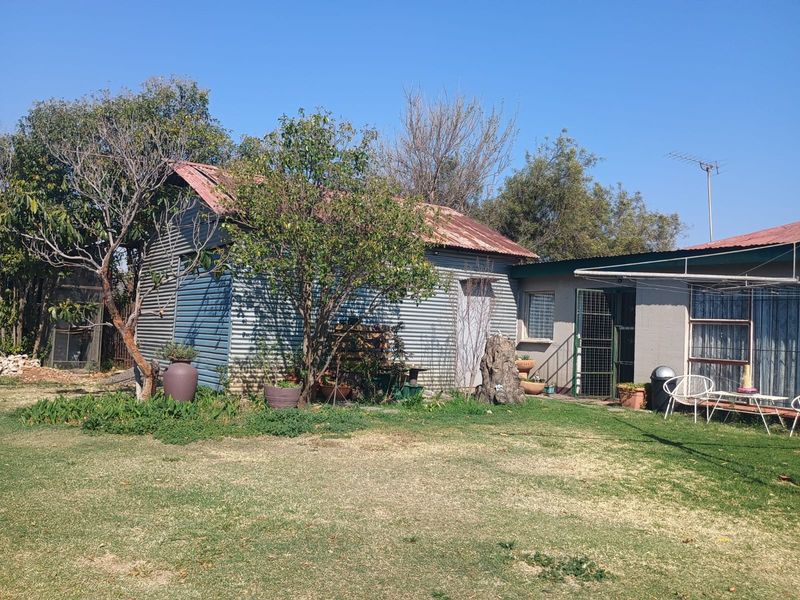 Rear view of the property featuring a corrugated iron structure with a rusted roof and a surrounding garden area.