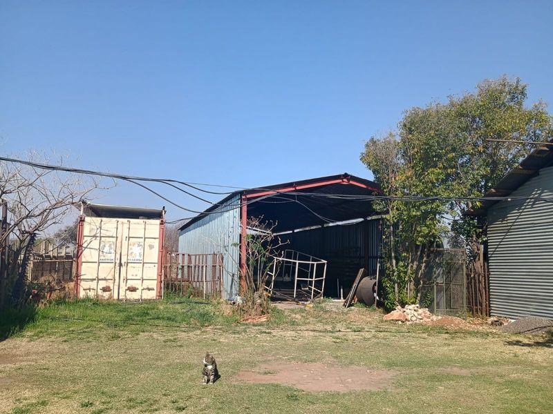 Rear yard area featuring a large corrugated metal shed, a shipping container, and basic fencing on a small holding property.