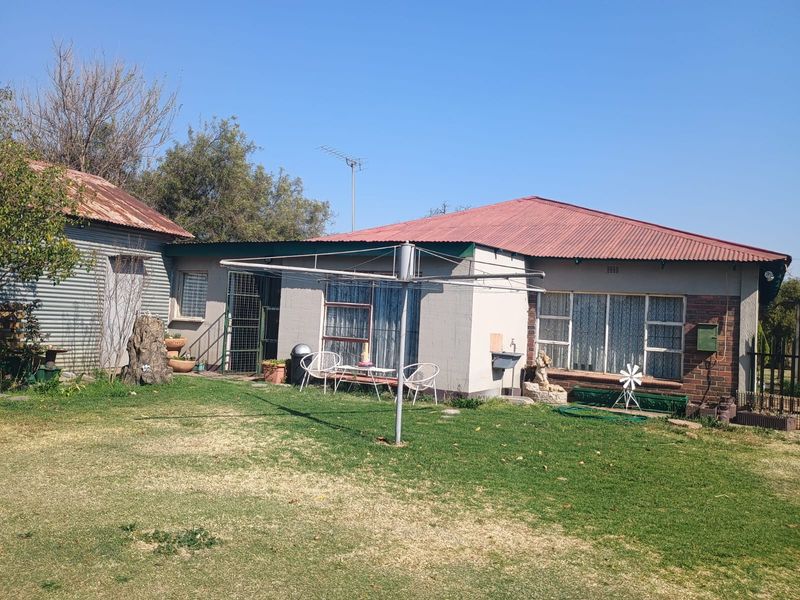 Rear view of the property showing a single-story dwelling with a corrugated iron roof, brick and plastered exterior walls, and established garden area.