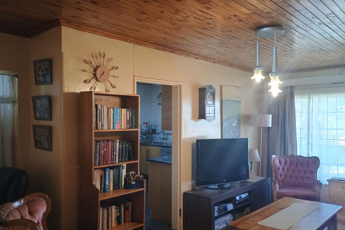 A living room featuring a traditional knotty pine wood ceiling and pendant lighting, with an open doorway leading into the kitchen area.