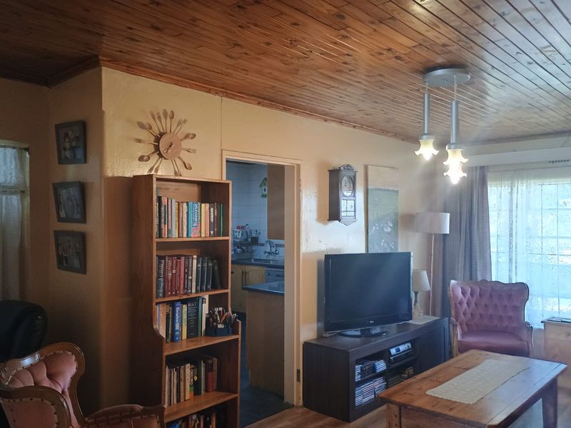 A living room featuring a traditional knotty pine wood ceiling and pendant lighting, with an open doorway leading into the kitchen area.