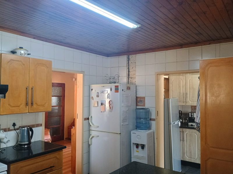 A dated kitchen featuring timber ceilings, tiled walls, and granite countertops, with an adjacent scullery area visible through the doorway.