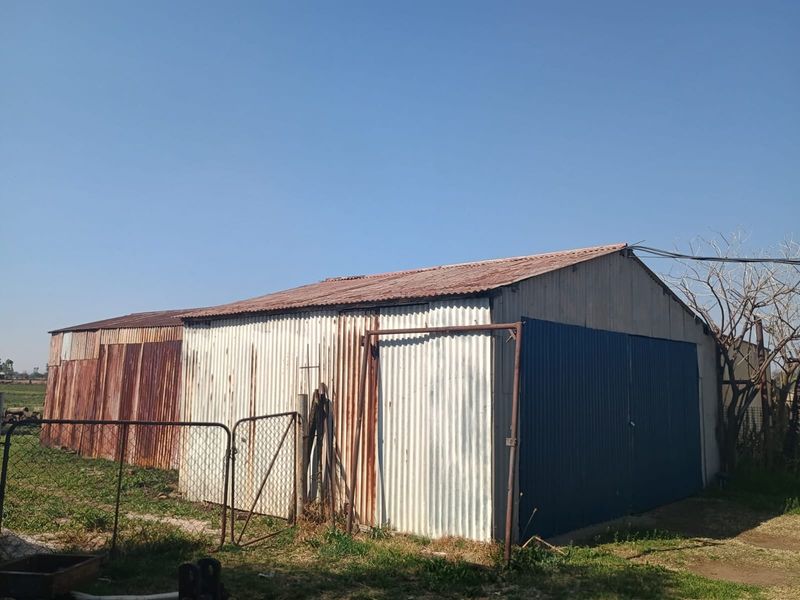 A detached utility shed or storage structure featuring corrugated iron walls and roofing, showing significant signs of weathering and surface rust.