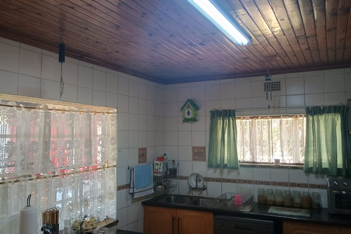 A functional kitchen featuring wooden ceiling paneling, tiled walls, and built-in cabinetry with a double sink and granite-style countertops.