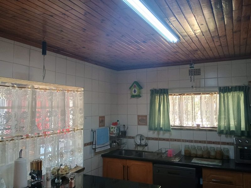 A functional kitchen featuring wooden ceiling paneling, tiled walls, and built-in cabinetry with a double sink and granite-style countertops.