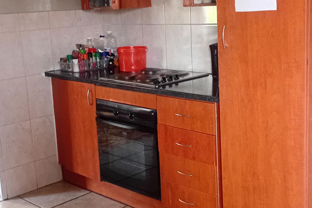 A functional kitchen featuring wooden cabinetry, a built-in oven, electric hob, extractor fan, and tiled finishes.