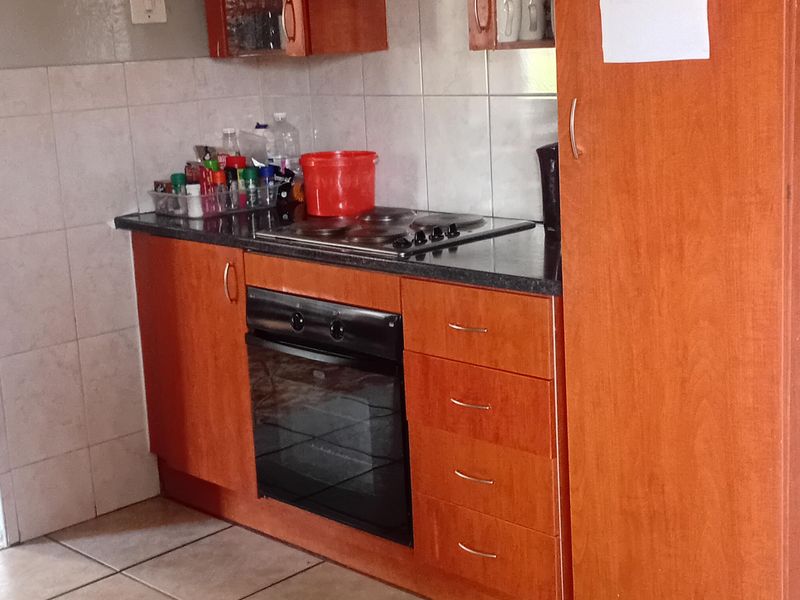 A functional kitchen featuring wooden cabinetry, a built-in oven, electric hob, extractor fan, and tiled finishes.