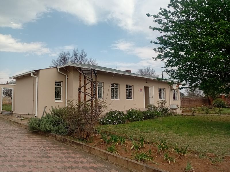 A single-story residential property featuring a paved driveway, security-barred windows, and a surrounding garden area.
