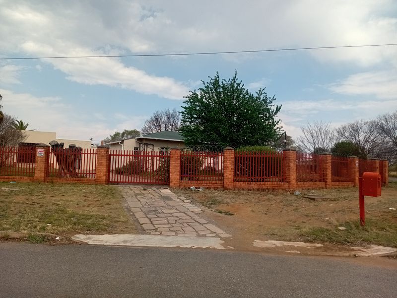 Front view of the property featuring a brick perimeter wall with steel palisade fencing, a secure driveway gate, and a stone paved entrance path.