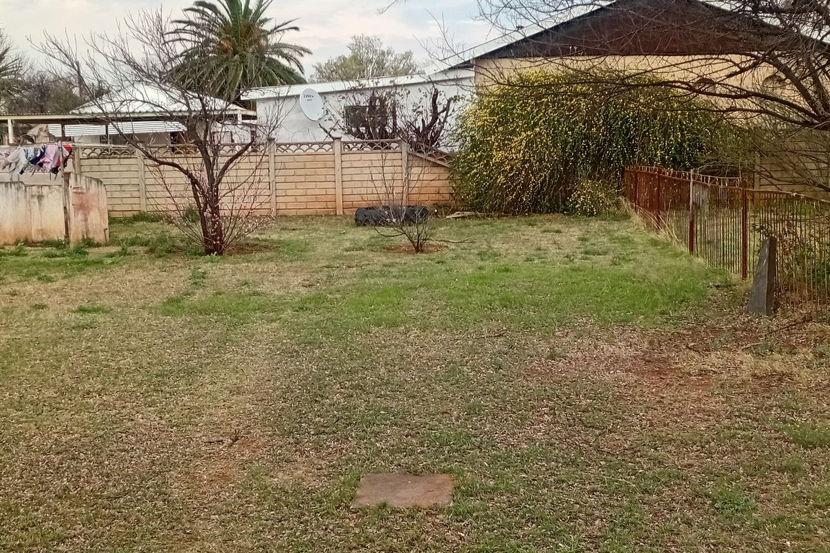 A rear garden area featuring a precast concrete boundary wall, metal fencing, and established trees, requiring landscaping maintenance.