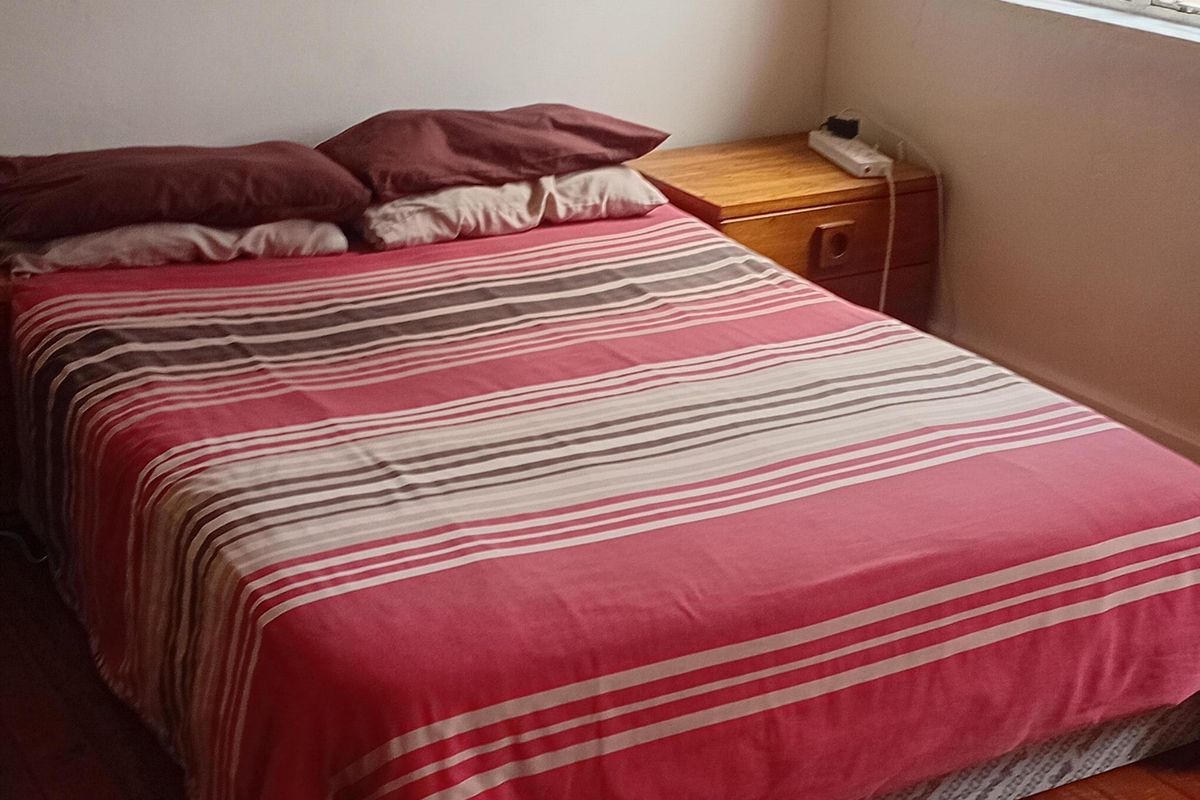A bedroom featuring polished timber flooring and a window fitted with security bars, providing natural light.