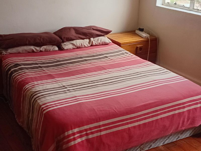 A bedroom featuring polished timber flooring and a window fitted with security bars, providing natural light.