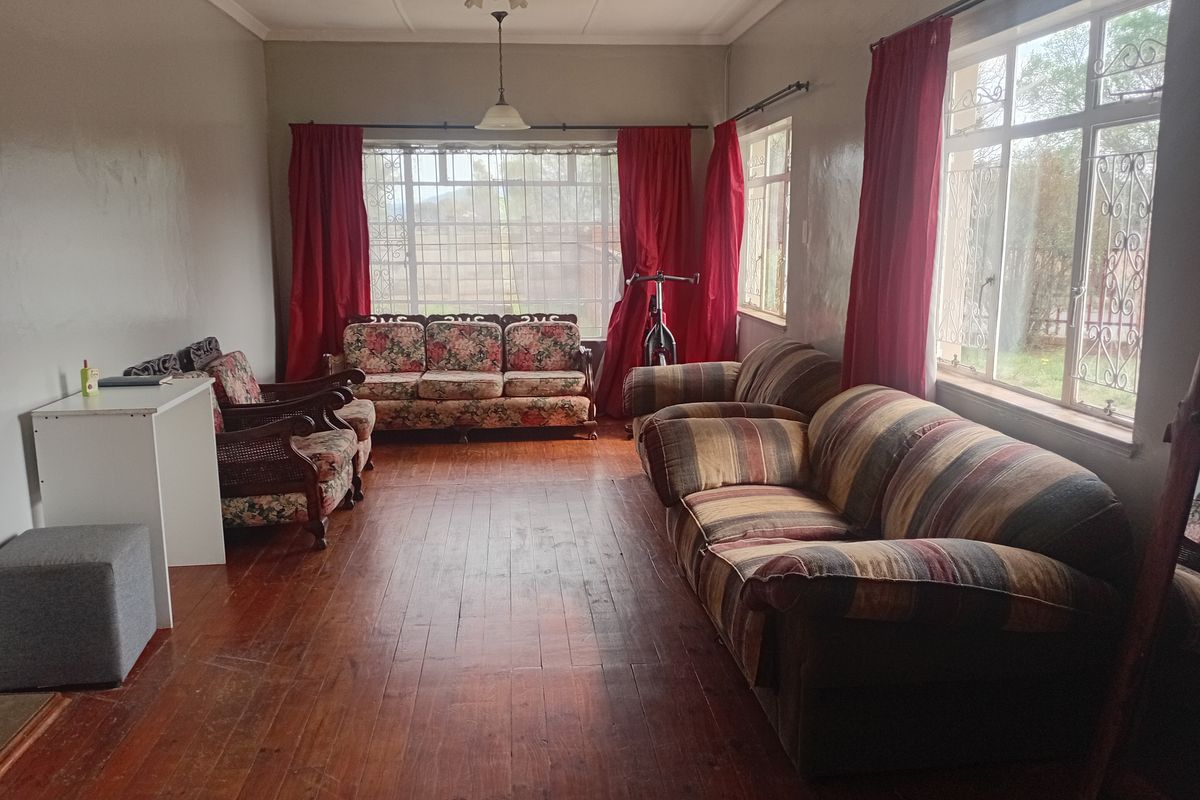 Spacious living room featuring original hardwood flooring, large windows with security bars, and a ceiling fan, offering a bright and traditional living space.