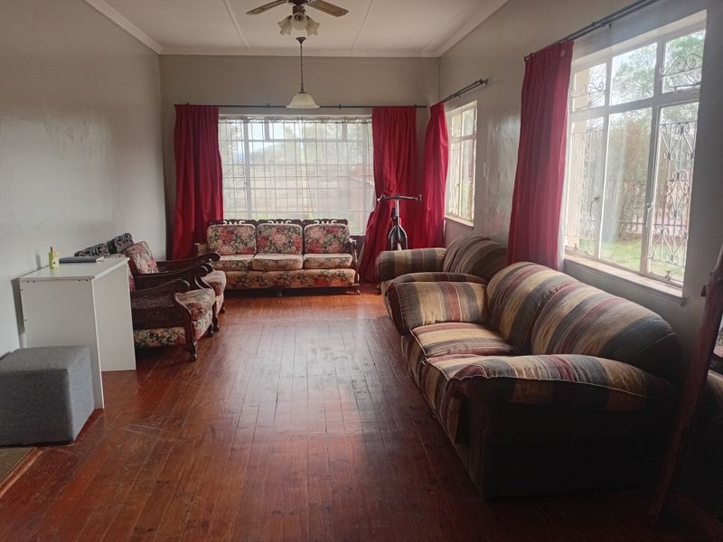 Spacious living room featuring original hardwood flooring, large windows with security bars, and a ceiling fan, offering a bright and traditional living space.