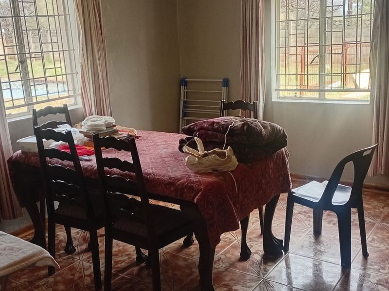 A dining room featuring tiled flooring and large windows with security bars, providing natural light and views of the exterior.
