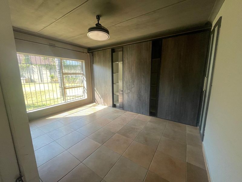 Spacious bedroom featuring large built-in cupboards, neutral tiled flooring, and natural light through windows fitted with security bars.