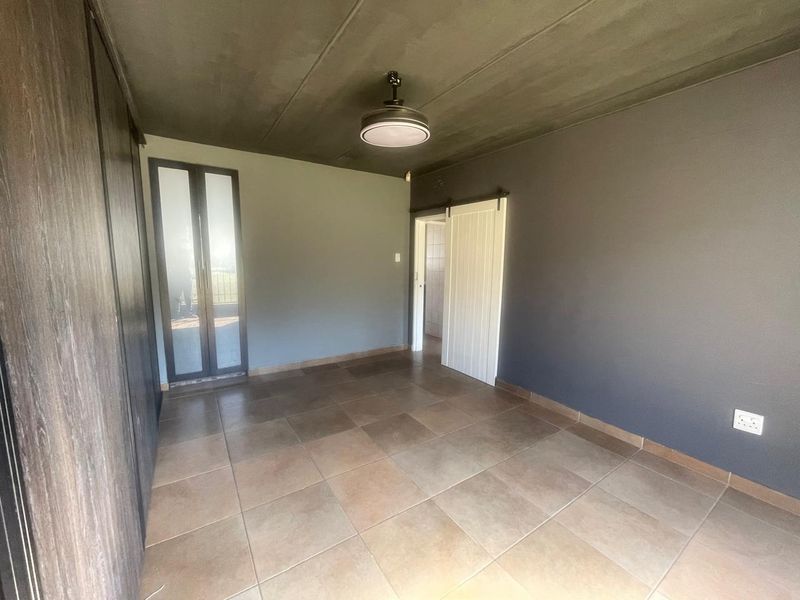 An empty bedroom featuring tiled flooring, built-in cupboards, a sliding barn door, and a neutral grey wall finish.