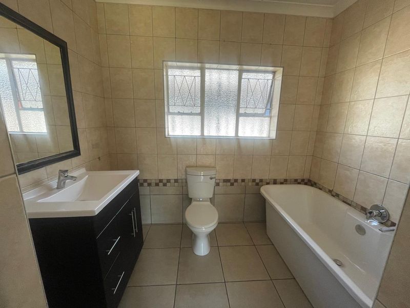 A functional bathroom featuring a vanity cabinet with basin, a standard toilet, and a bathtub, finished with neutral wall and floor tiling.