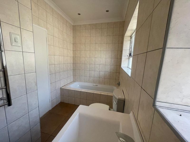 A functional bathroom featuring tiled walls and flooring, a built-in bathtub, a toilet, and a basin, offering a clean and neutral space.