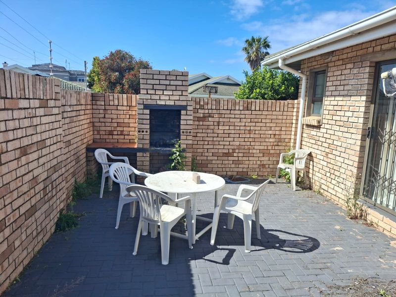 A private outdoor patio area featuring a built-in brick braai, paved flooring, and enclosed by brick boundary walls, accessible via a sliding door.