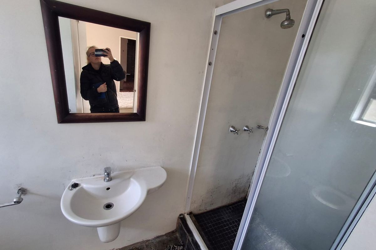 A compact bathroom featuring a wall-mounted basin and a separate shower enclosure, currently requiring maintenance and cosmetic updates to improve its condition.