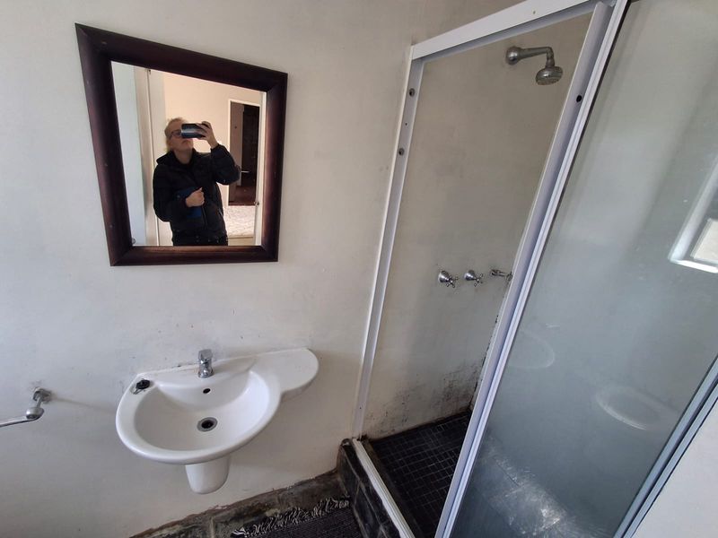 A compact bathroom featuring a wall-mounted basin and a separate shower enclosure, currently requiring maintenance and cosmetic updates to improve its condition.
