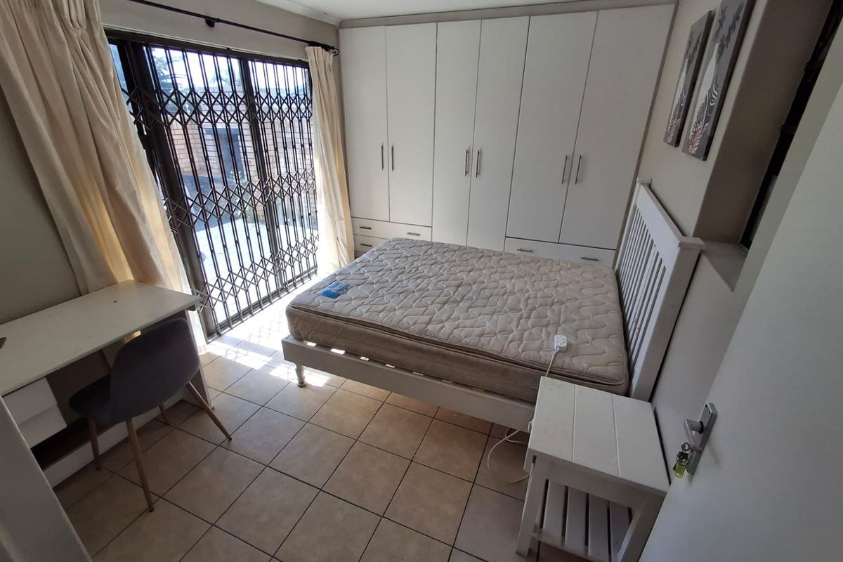 A bedroom featuring built-in cupboards, tiled flooring, and a sliding door with a security gate leading to the exterior.